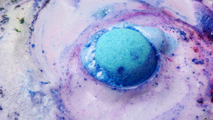 melting bath bomb, in vivid turquoise color, vivid bath balls, dissolving in pale purple foamy liquid, blue and dark purple, violet and red