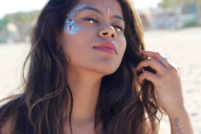 wavy dark brunette hair, and blue face paint with red and silver details, worn by young woman, with closed eyes and two star stickers