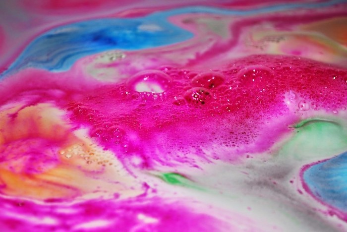 foamy liquid in bright vivid colors, hot pink and azure blue, pale orange and green, frothy white streaks and bubbles, dissolved bath bomb in rainbow colors