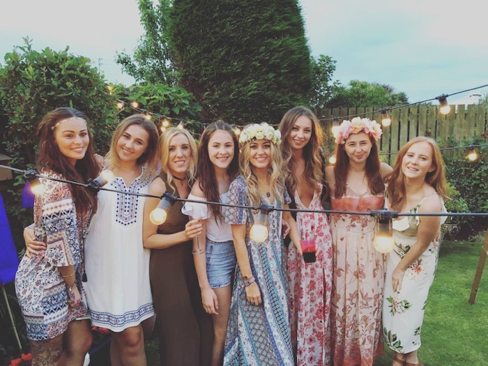 eight young women, dressed in multicolored patterned maxi dresses, folk-inspired boho tunics, denim shorts and a white top, casual dress code, smiling and posing for a photo