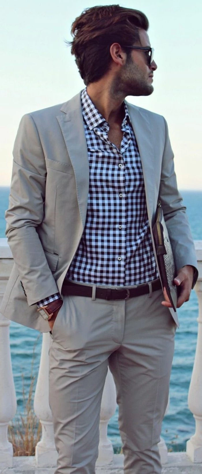 beige two piece suit, worn with blue and white checkered shirt, by brunette man, mens casual summer wedding attire, with glasses and a hand in his pocket