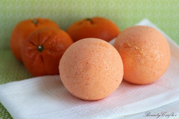 napkin in white, with two pale orange bath bombs, three clementine oranges in the background