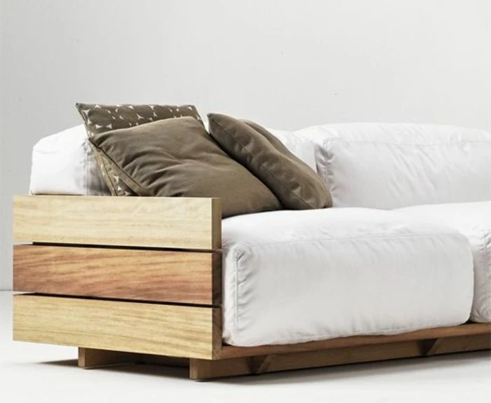 three beige pillows, decorating a diy sofa, made from wooden pallets, with off-white couch cushions, white floor and background