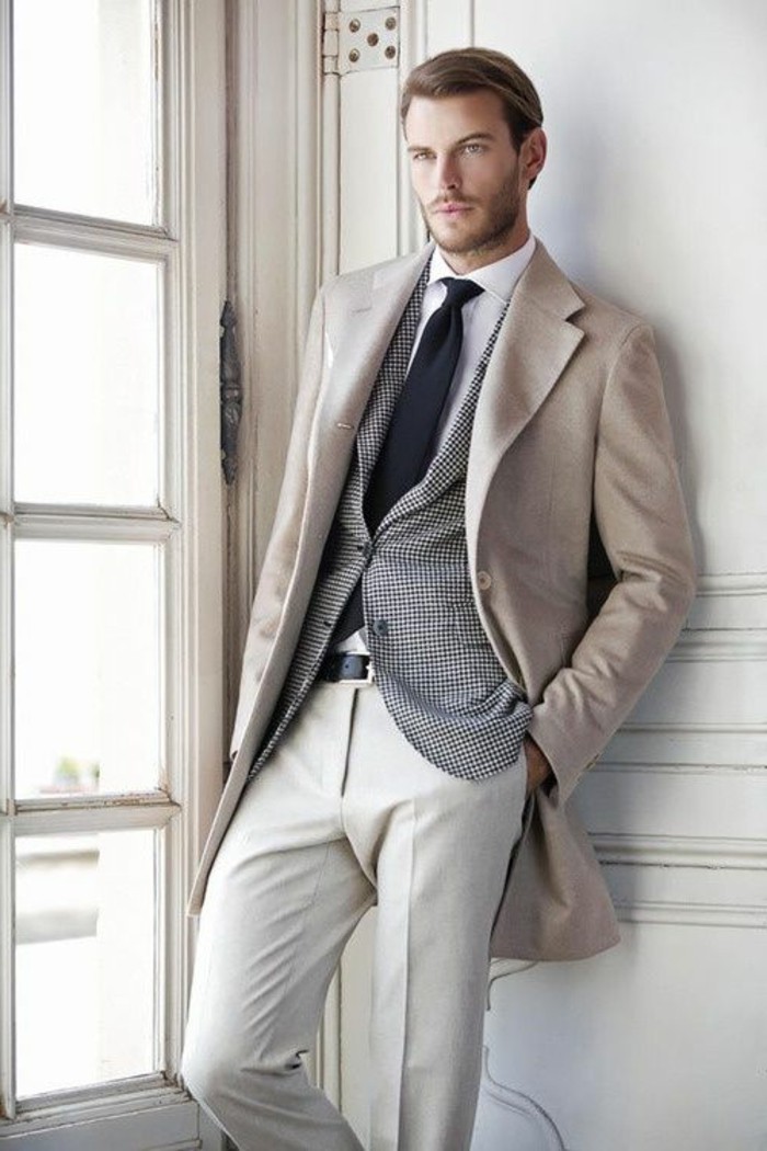 woolen coat in cream, worn by young man, with white shirt and black tie, striped blazer and white trousers, how to dress for a wedding male, leaning on a wall