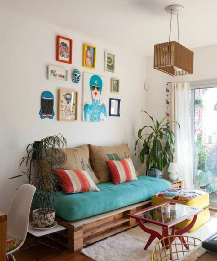 potted plants and colorful framed artworks, near a diy pallet couch, decorated with a large turquoise pillow, and several cushions