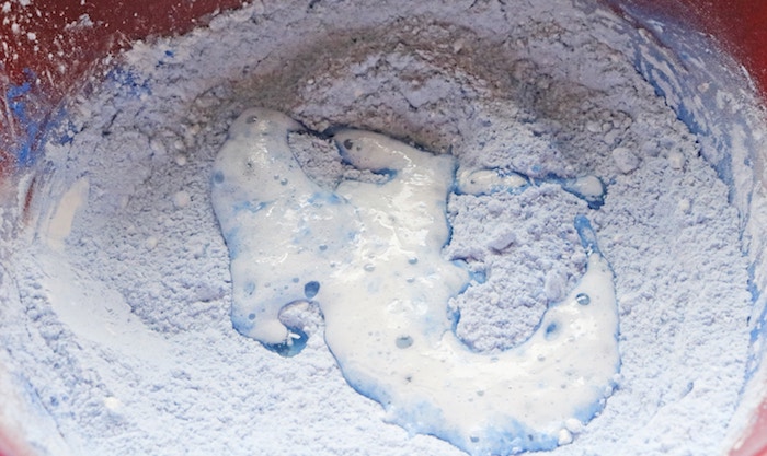 mixing white and blue powder, to form light blue mixture, and adding liquid, how to make bath bombs, inside a plastic red mixing bowl