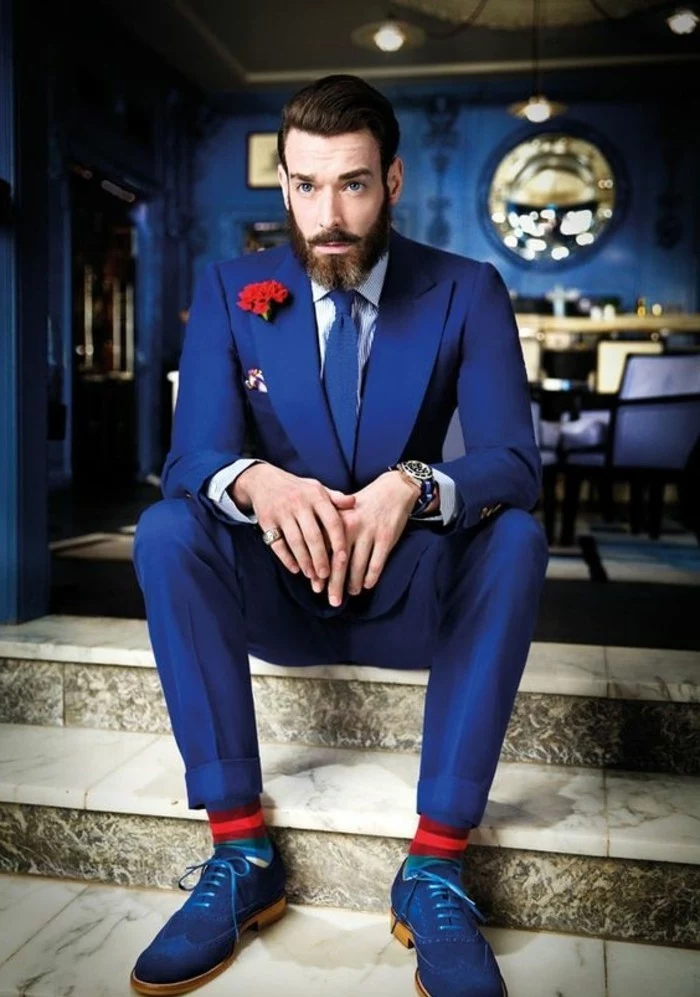 accents in red, worn by a bearded man, in a vivid blue suit, with white shirt, blue shoes and a blue tie, red boutonniere and socks