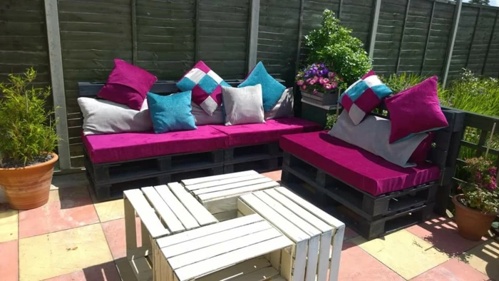 garden with furniture made from pallets, black painted wooden pallets, covered with fuchsia sofa cushions, and smaller cushions, in different colors and patterns