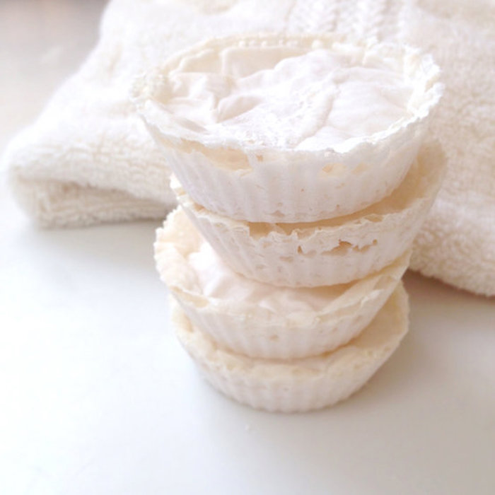 stacked foamy bath bombs, in creamy white, made to look like little tartlets, placed on white surface, near a white fluffy towel