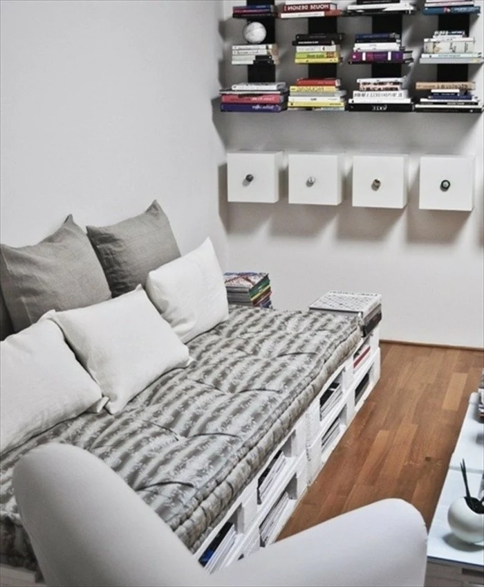 grey and white couch, made from white painted pallets, and textiles in soft grey tones, how to make pallet furniture, several bookshelves nearby