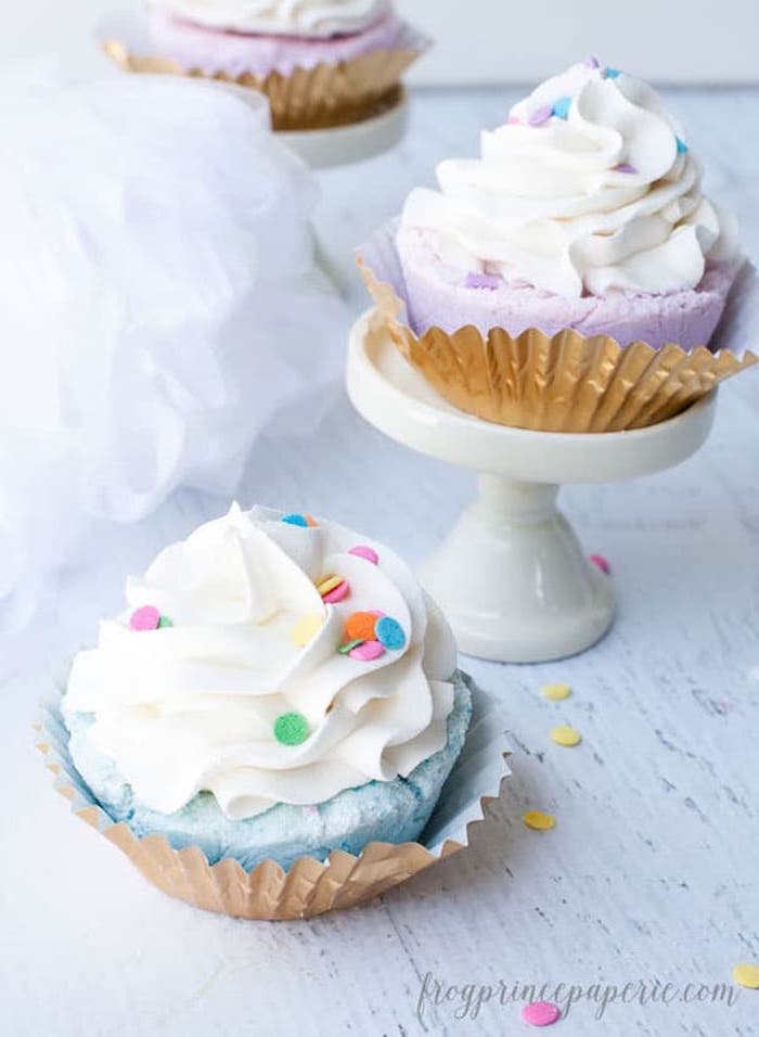 frosted cupcake-style homemade bath bombs, in blue and pink, with white topping, and decorated with multicolored confetti