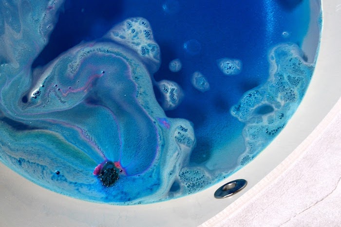 frothy dark blue water, with pale blue and white foam, dark purple tint, melted bath bomb, inside a white bathtub