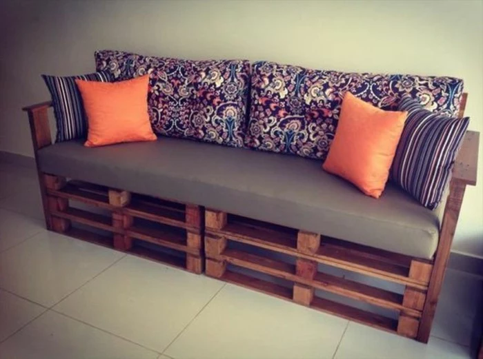 folk-inspired dark floral pattern, on the backrest cushions, of a diy sofa, made from dark brown wooden pallets, decorated with two sets of cushions