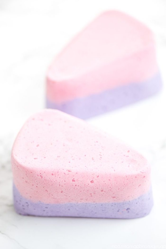 two-tone diy bath bombs, in pale pastel pink and violet, shaped like cake slices, and placed on a pale marble surface