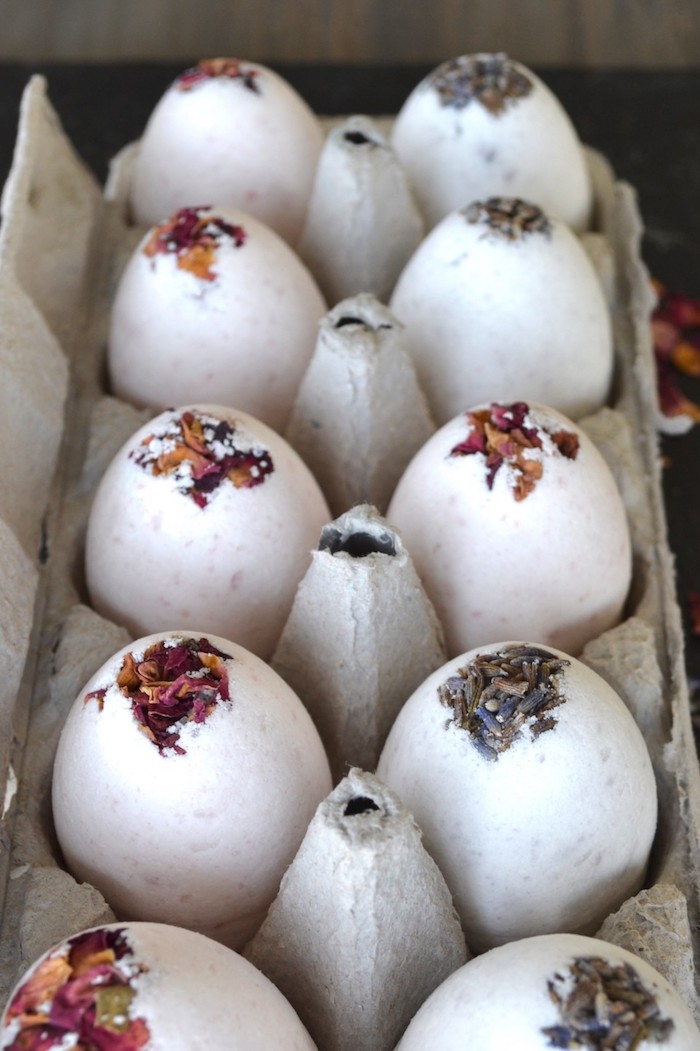 ten egg shaped bath bombs, decorated with dried rose and lavender petals on top, placed inside a grey cardboard box