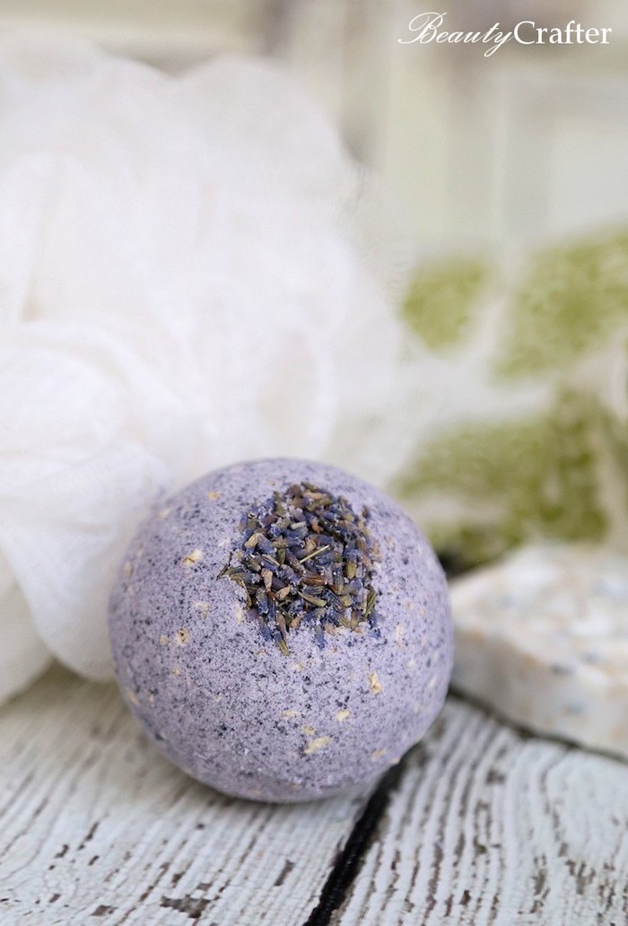 lavender bath bomb, pale violet in color, and spherical in shape, decorated with dried lavender petals, and placed on wooden surface