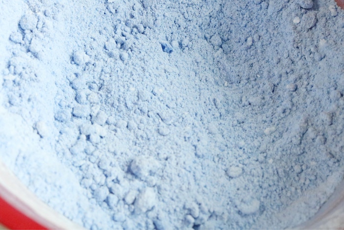 light blue fine powder, with small lumps, inside a plastic mixing bowl, in red and white, how to make bath bombs, ingredients seen in close up