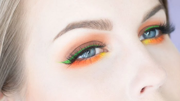 bright green yellow and orange eyeshadow, festival makeup, decorating the blue eyes of a pale woman, with ash blonde hair