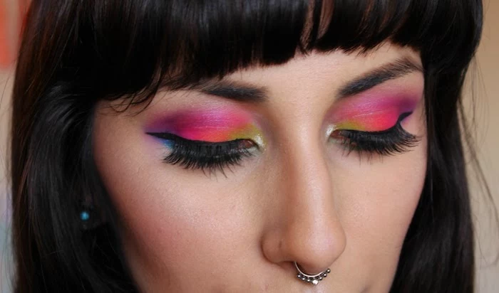 silver nose ring, worn by woman with dark hair and bangs, wearing fake lashes, makeup ideas, black eyeliner and eyeshadow, in yellow and orange, pink purple and blue