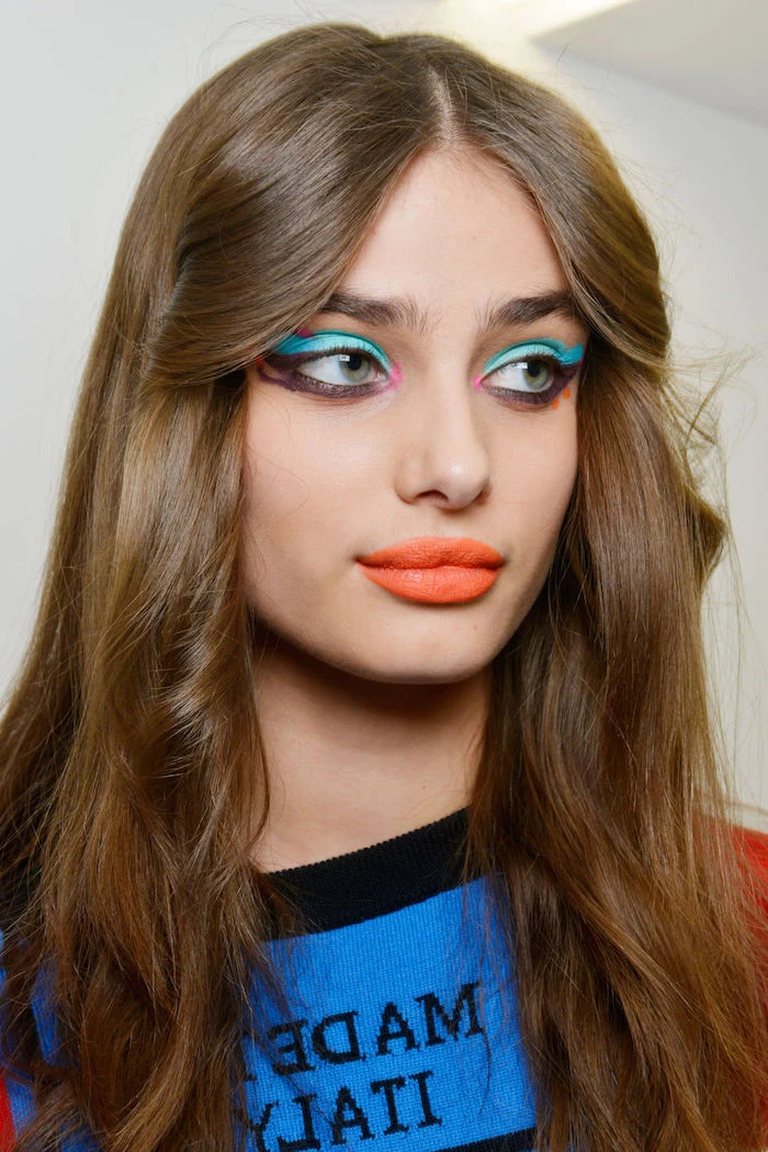 turquoise and black eyeliner, worn by famous model, with brunette hair, and bright orange lipstick, blue and black top, makeup ideas