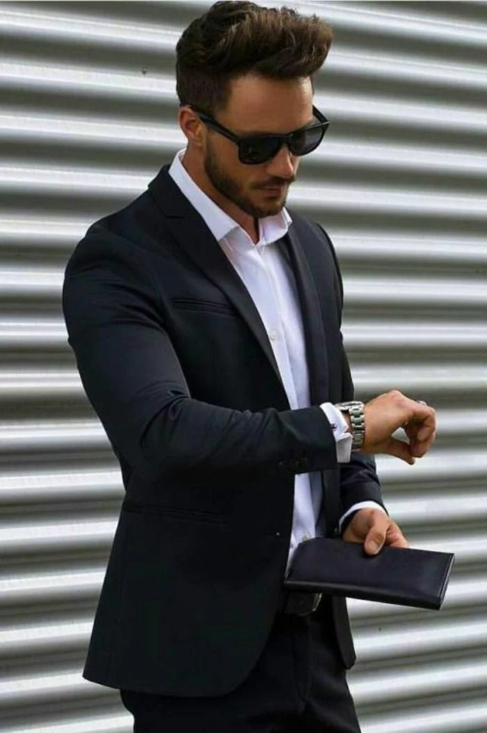 classical black suit, worn with a white shirt, by young man with sunglasses, black tie optional wedding, holding a black leather wallet, and looking at his watch