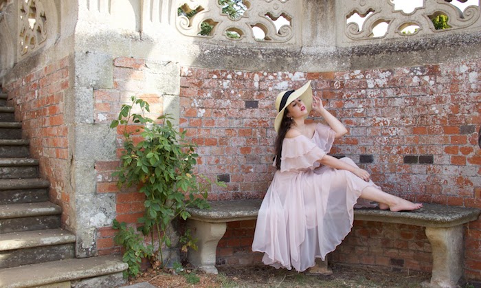 what is semi formal, barefoot young woman, with long dark brunette hair, wearing a floaty semi-sheer powder pink dress, with ruffles and a large straw hat, with a black ribbon