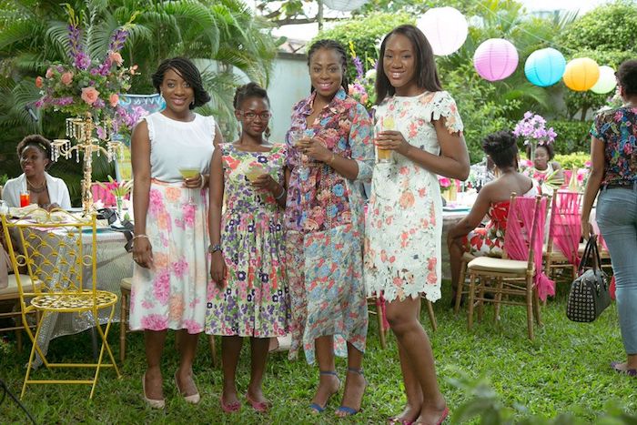 four young women, wearing multicolored floral print dresses, in different lengths and styles, dressy casual, garden party in the background