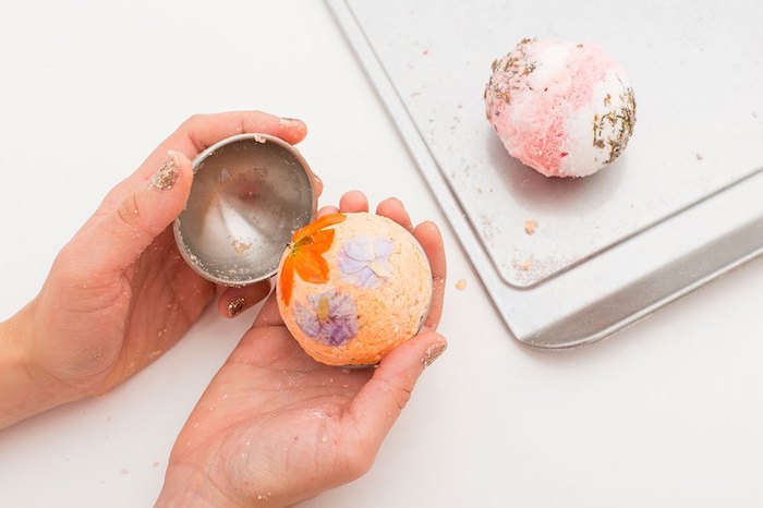 taking a light orange bath bomb, decorated with pale violet and vibrant orange, out from a metal mould, how to use a bath bomb, another ready pink bath bomb nearby