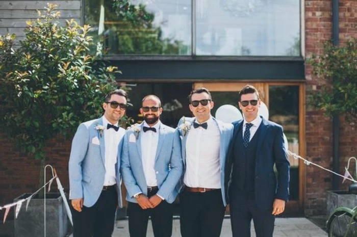 coordinated outfits on three men, pale blue blazers, white shirts and black bowties, mens wedding guest attire, standing next to the groom