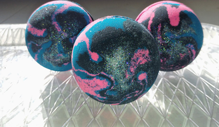 sparkly black bath balls, with and dark pink and blue streaks, like small galaxies, a total of three, placed on a glass surface