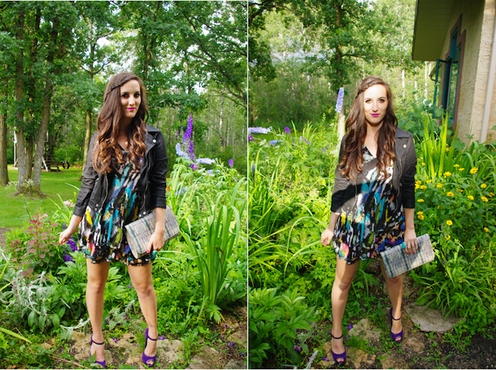 leather biker jacket in black, worn over multicolored mini dress, smiling brunette woman in dressy casual style, with purple high heel sandals, holding a large clutch bag