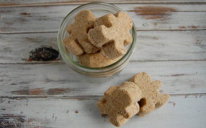 cookie-like beige gingerbread men bath bombs, some placed in a small glass bowl, some lying on the table nearby