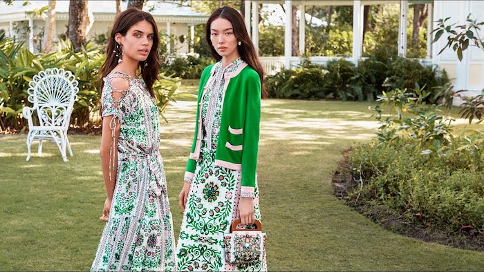 two young brunette women, wearing maxi dresses in green and white, decorated with floral patterns, and other colors, what is semi formal, green and pink cardigan, and small retro bag