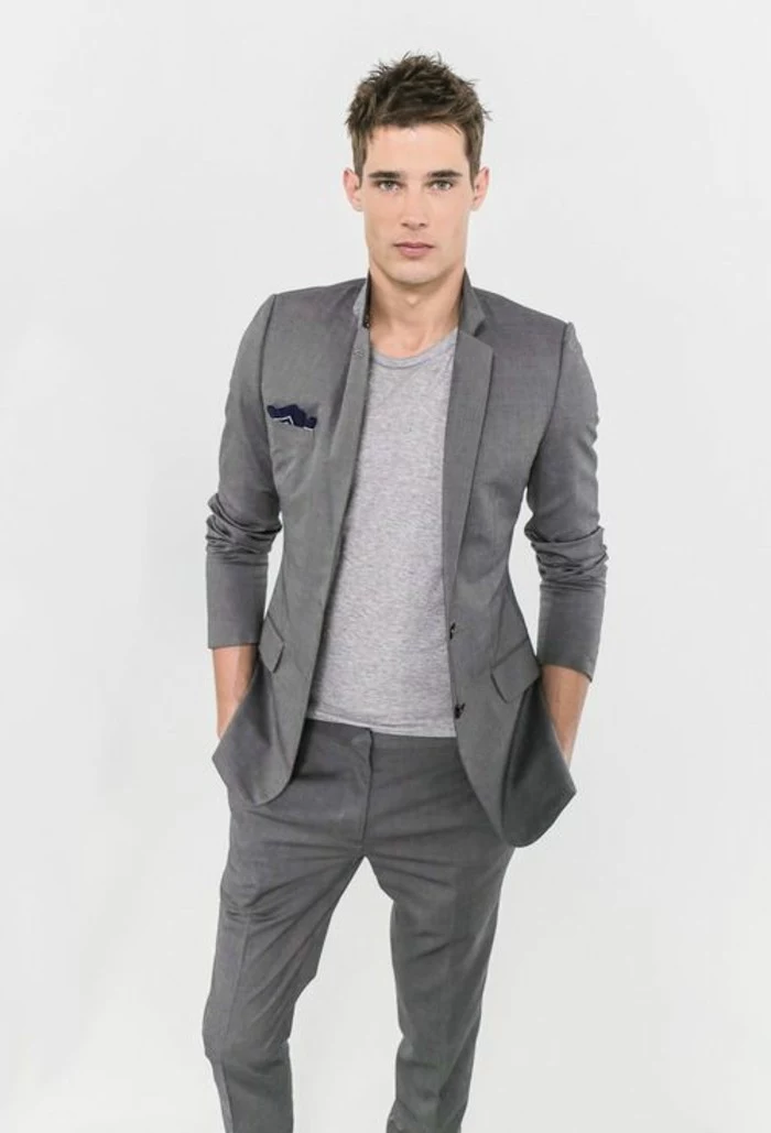 t-shirt in pale grey, worn with a dark grey suit, by young man, with hands in his jacket pockets, mens casual summer wedding attire, plain white background