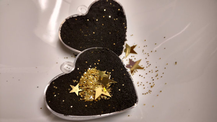 golden shiny star-shaped confetti, and glitter in the same color, inside a heart-shaped mould, filled with black powder, making a black bath bomb 