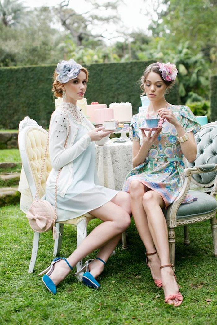 semi formal dress code, two young women, having tea in a garden, wearing silky mini dresses, in pastel colors, with matching shoes, and hair ornaments