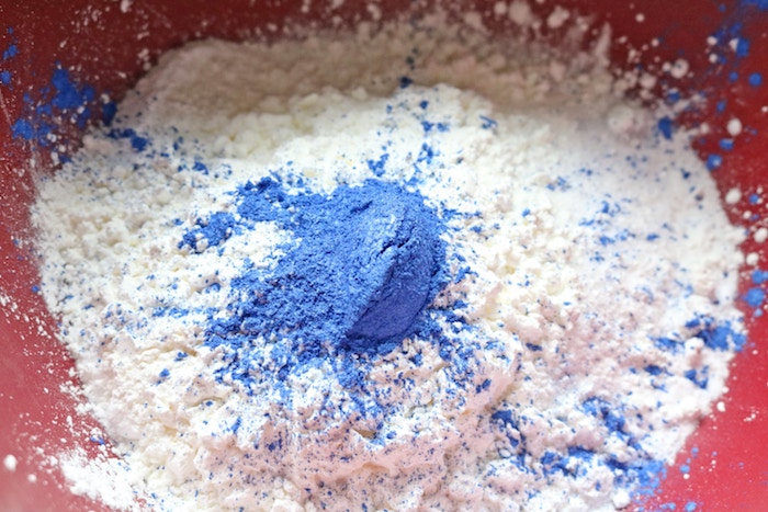 fine blue powder, on top of lumpy white powder, how to make bath bombs, ingredients inside a red plastic mixing bowl
