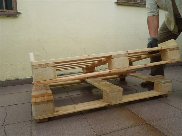 man ing grayish clothing, putting half of a wooden pallet, on top of a whole pallet, how to make pallet furniture 