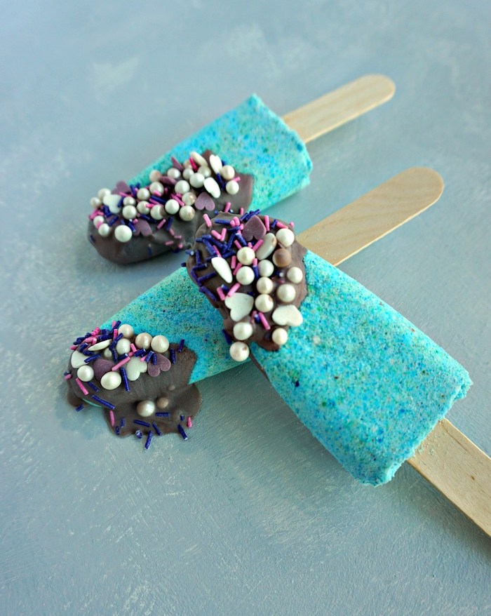 turquoise homemade bath bombs, shaped like ice creams on a stick, three in total, decorated with chocolate-like frosting, pearls and sprinkles