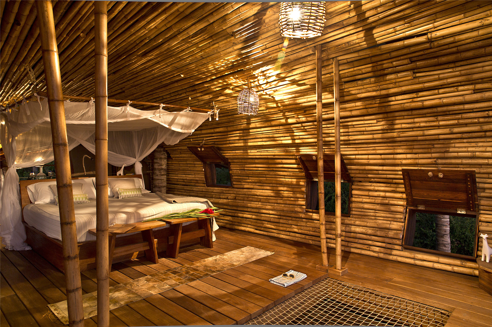 diy treehouse made from bamboo and wood, double bed with a baldachin, several lit lamps, three windows with open shutters