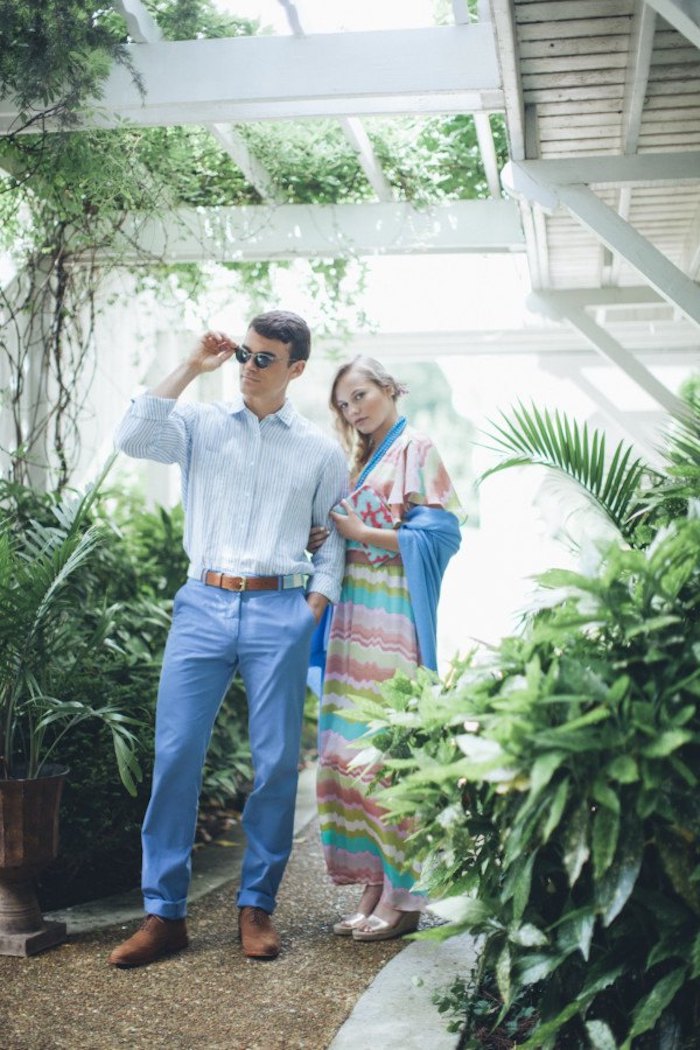 blue trousers and pale blue shirt, worn with brown shoes and sunglasses, by brunette man, standing next to blonde woman, in striped multicolored maxi dress, dressy casual men