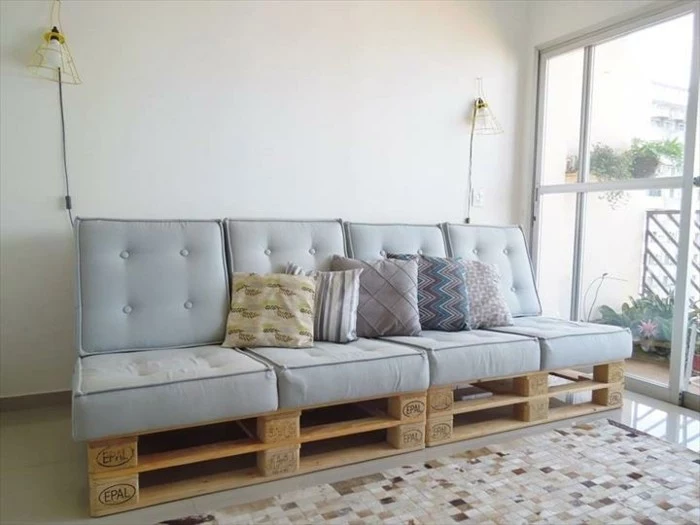 pale duck's egg blue pillows, covering a sofa made of pallets, with several cushions in different patterns, large window nearby