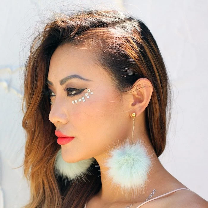 fluffy pale blue earrings, worn by brunette woman, with auburn strands in her hair, black eyeliner and bright, neon red lipstick, silver pearl stickers under here eye