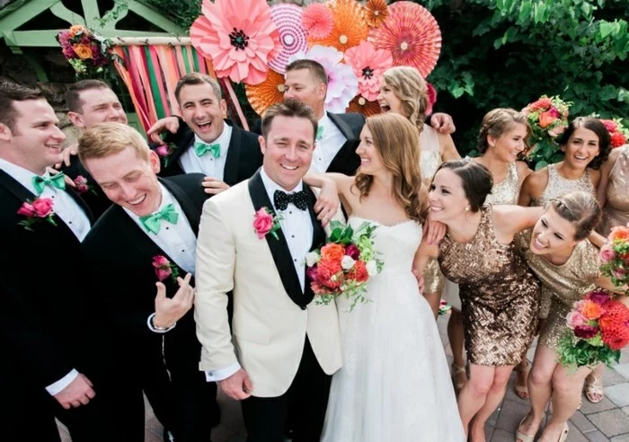 smiling bride and groom, surrounded by several men, dressed in black suits, with white shirts, and mint green bowties, mens summer wedding attire, bridesmaids dressed in golden sequin dresses