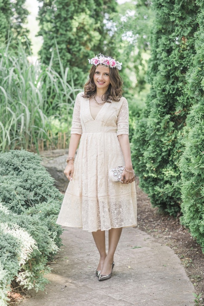 lace midi dress in cream, with 3/4 sleeves, worn with silver shoes, and a flower crown, by smiling brunette woman, holding a clutch bag, dressy casual