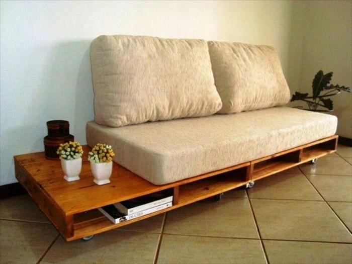 retro style diy sofa, made from polished wooden pallets, in a warm brown tone, with wheels and storage spaces, beige sofa cushions, and potted plants