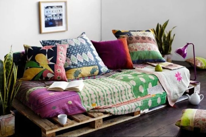 boho-style pallet sofa, covered in different textiles and cushions, in various colors and patterns, two potted plants nearby