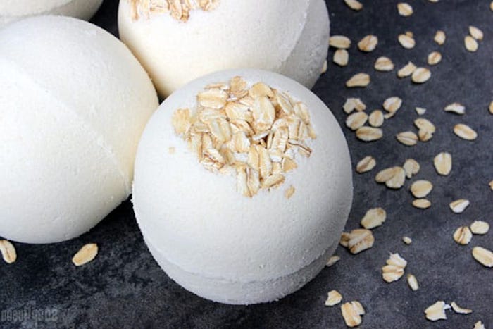 oats bath bombs, white and round, decorated with rolled oats on top, placed on a dark grey surface, with oatmeal flakes strewn about