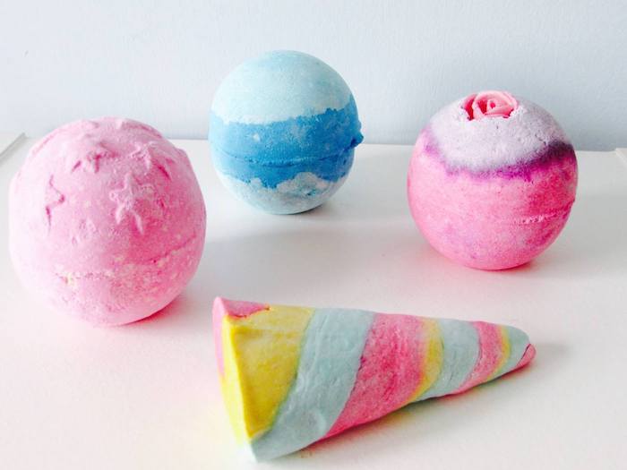 four bath bombs, three round and dyed in pale pink, light blue and purple, and one cone shaped, with swirly striped yellow, pale green and pink pattern