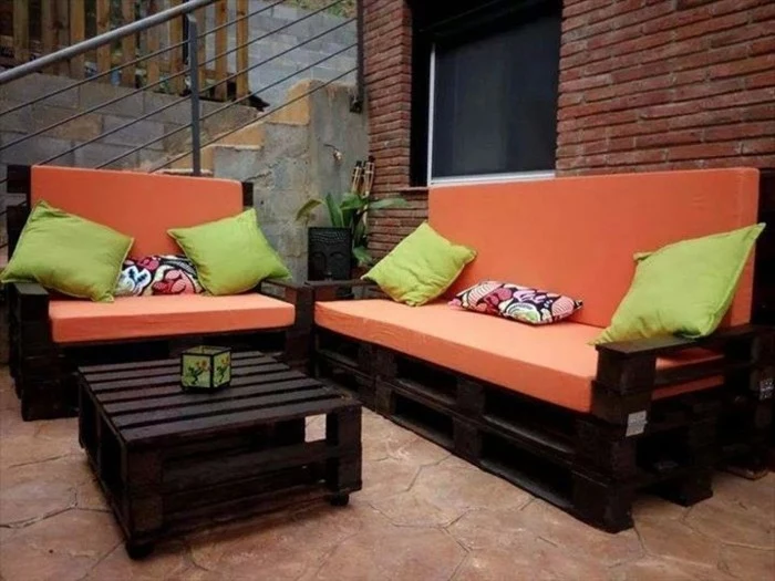 settee and sofa, made from dark wooden pallets, decorated with orange foam pillows, pallet patio furniture, light green and pink and white cushions